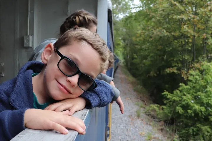 young boy wearing sunglasses looking out the open air car