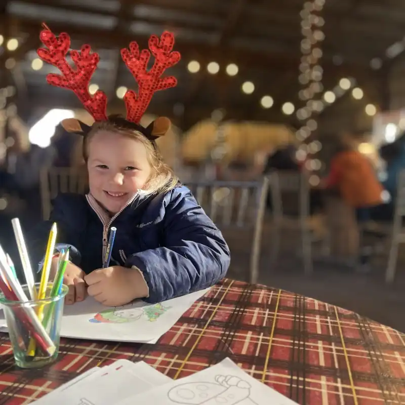 Little girl with raindeer antlers coloring at the Potomac Eagle event barn during the Christmas season